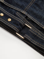 Cropped denim top with short sleeves, dark blue fabric, yellow stitching, brass buttons, metal buckle.