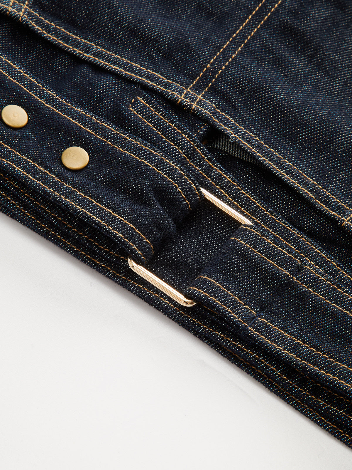 Cropped denim top with short sleeves, dark blue fabric, yellow stitching, brass buttons, metal buckle.