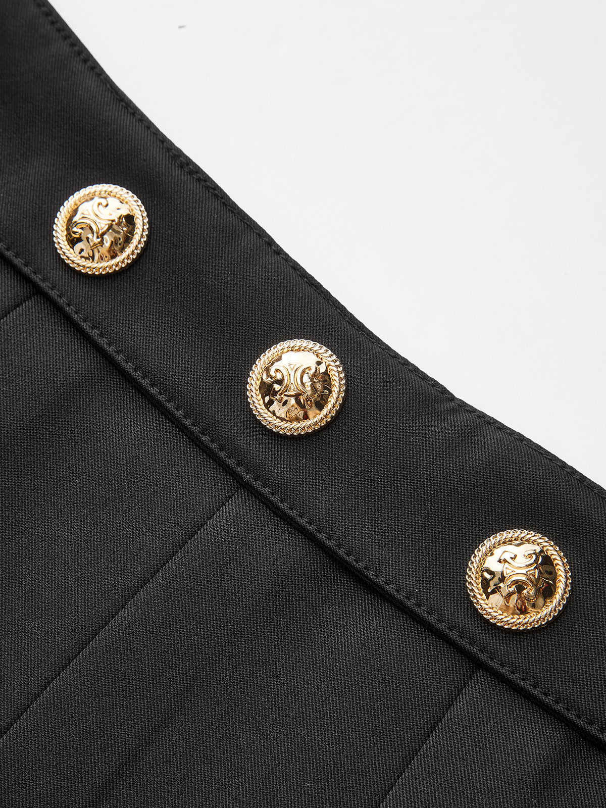 Black pleated mini skirt with three gold, embossed buttons featuring rope-like borders.