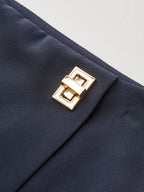 Navy blue asymmetrical skort featuring a shiny gold rectangular buckle and metallic accent.