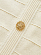 Cream stretch knit backless halter dress with vertical ribs and a single gold neck button.