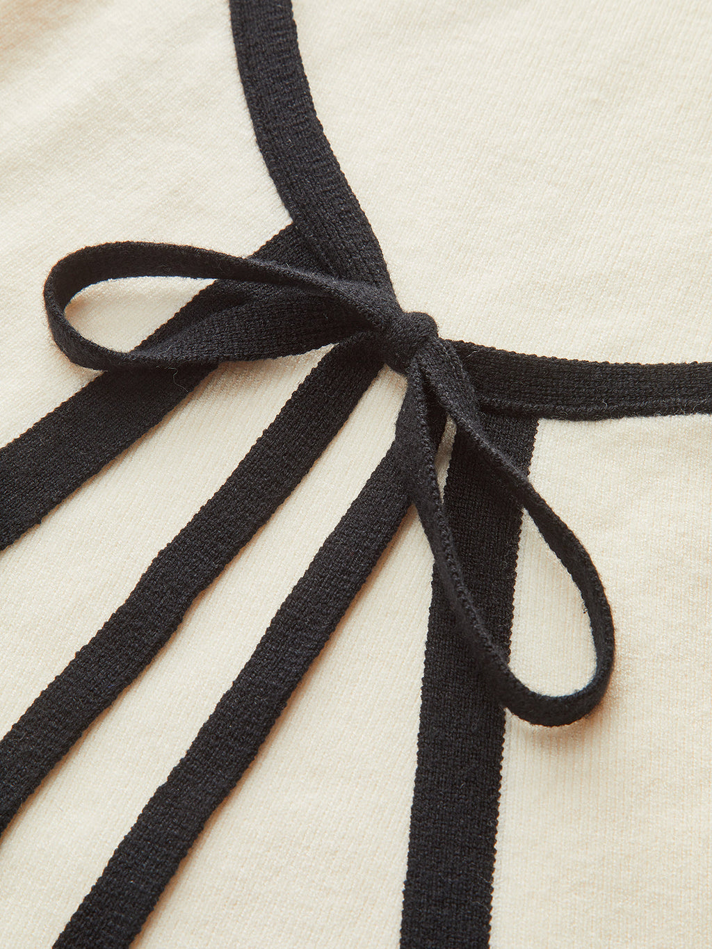 Cream mini sweater dress with long sleeves, black knit trim, and a black bow.
