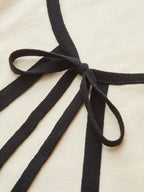 Cream mini sweater dress with long sleeves, black knit trim, and a black bow.