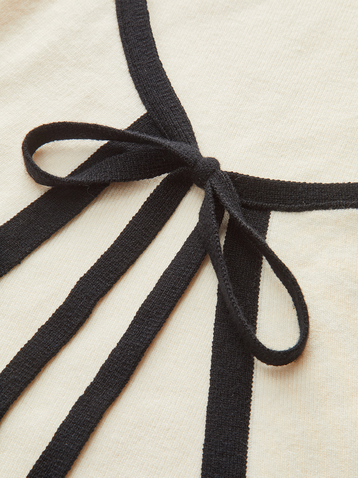 Cream mini sweater dress with long sleeves, black knit trim, and a black bow.