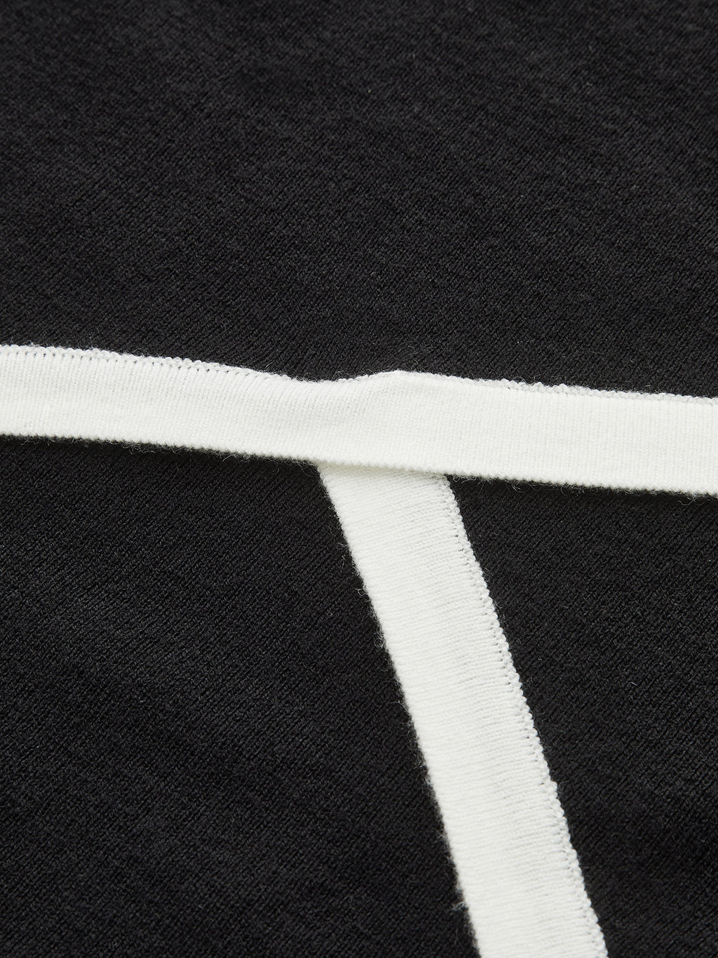 Black asymmetric wool blend polo crop with T-shaped white trim and textured knit fabric.