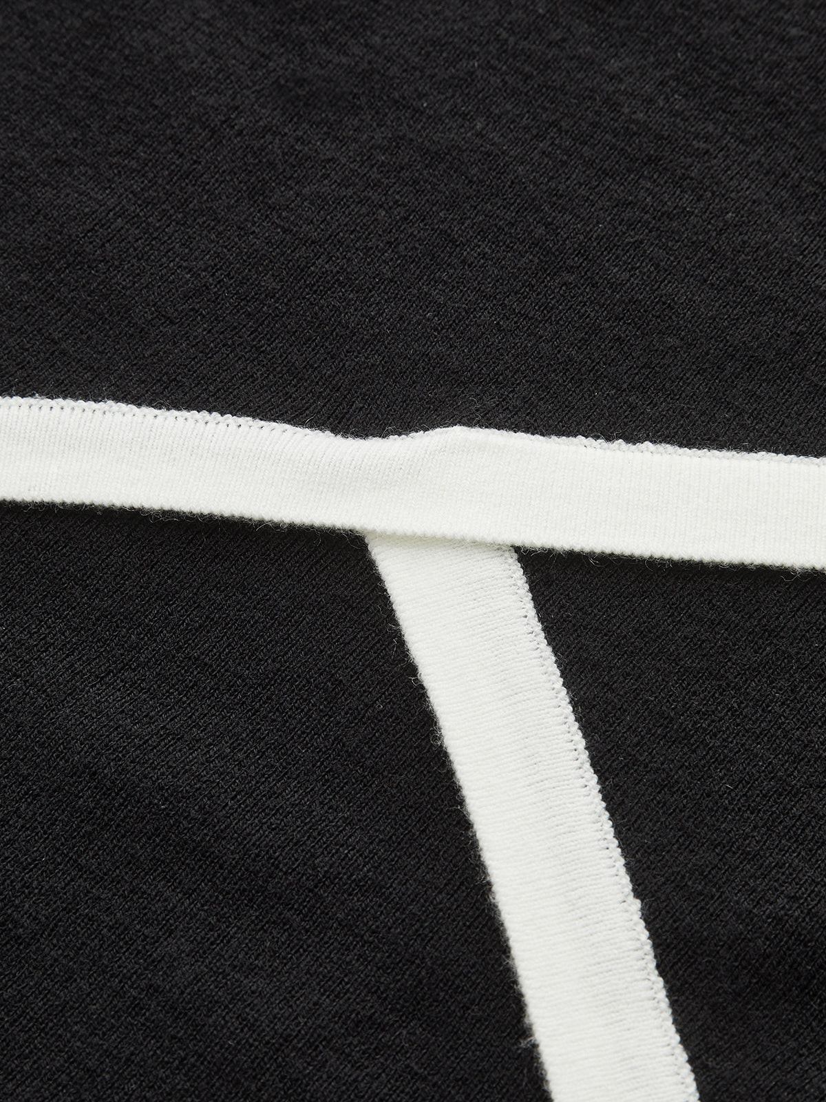 Black asymmetric wool blend polo crop with T-shaped white trim and textured knit fabric.