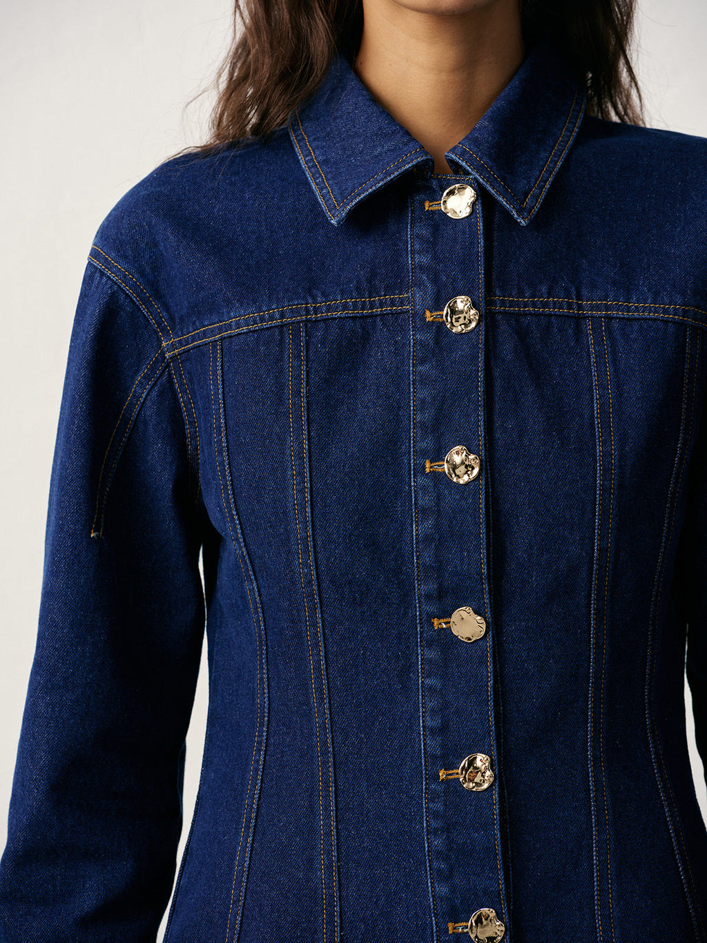 A 100 cotton fitted denim jacket with metal buttons, prominent stitching, and a pointed collar.