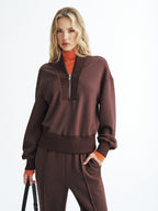 Brown LA FINE FLEUR V-neck half-zip cozy pullover over orange turtleneck and brown sweatpants.