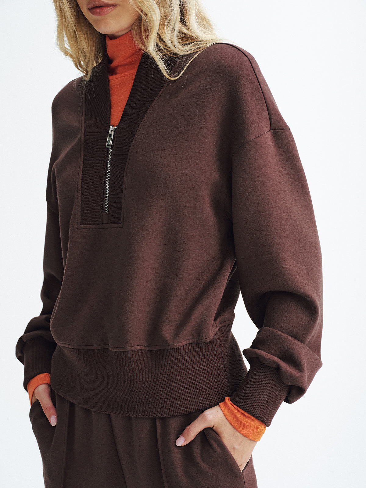 Brown V-neck half-zip pullover sweatshirt over an orange turtleneck and matching pants.