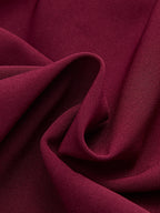 Sleeveless burgundy mini dress with asymmetric ruffle hem, woven fabric, soft folds, subtle texture.