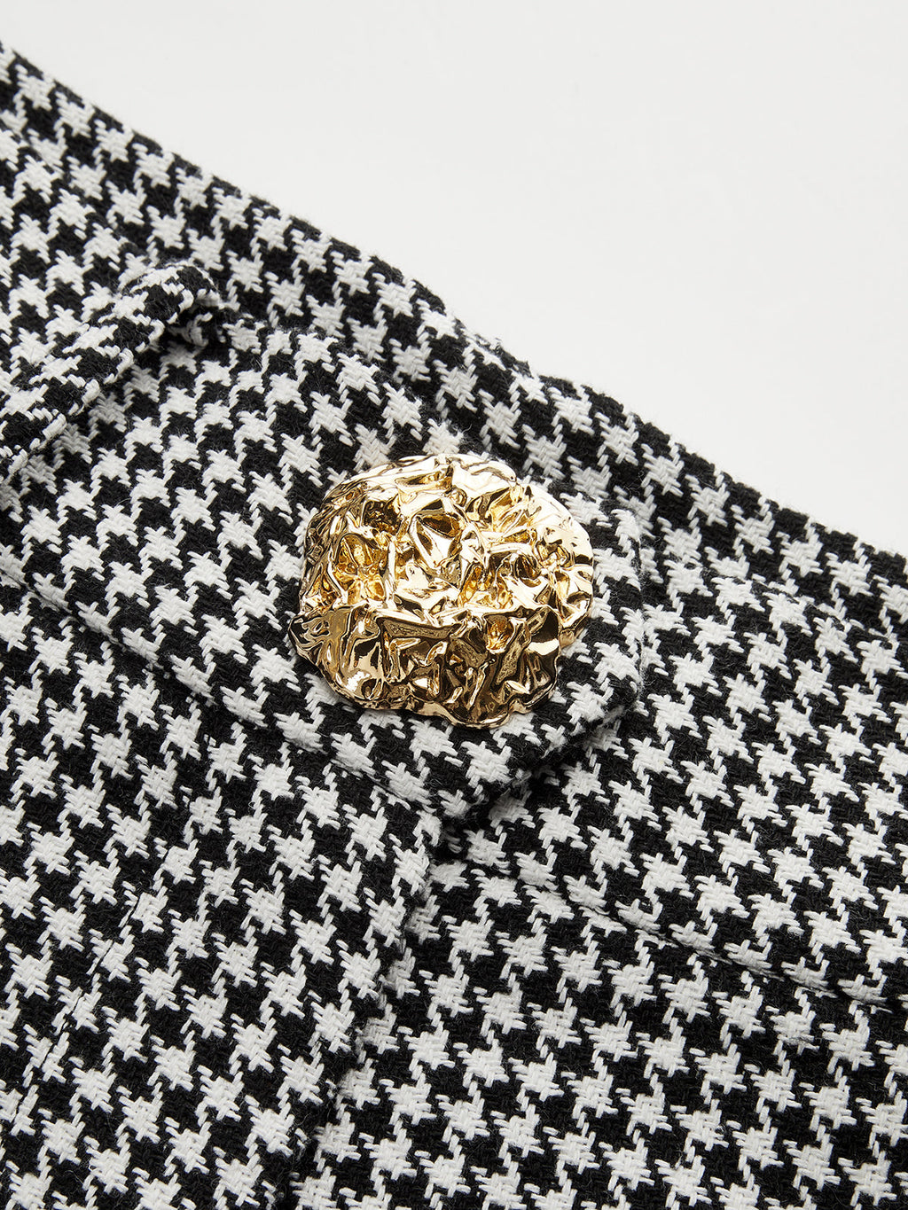 Close-up of houndstooth pleated wide leg pants with a textured, irregular gold button.