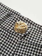 Close-up of houndstooth pleated wide leg pants with a textured, irregular gold button.