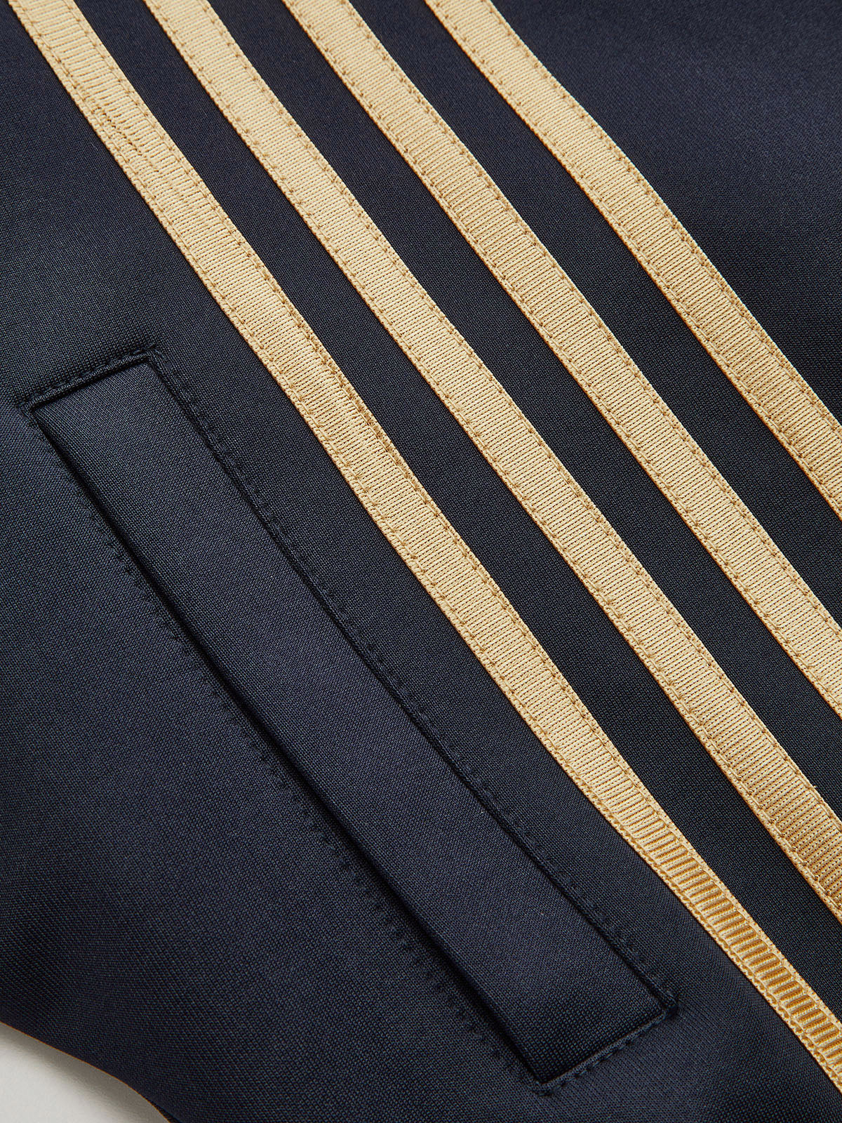 Black cropped athletic sweatshirt with four gold stripes and a rectangular pocket on front.