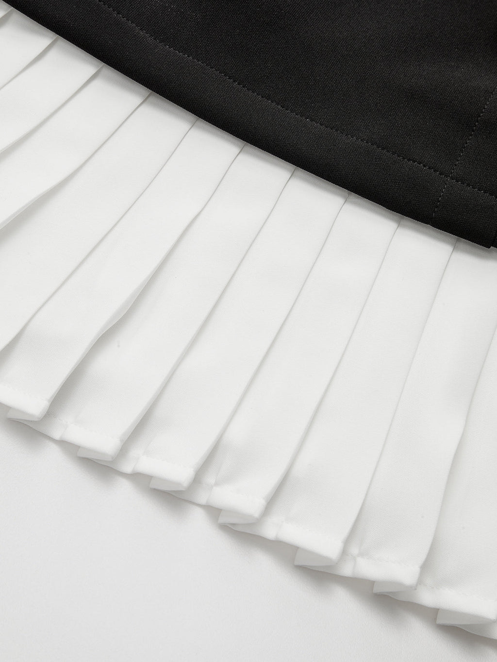 Asymmetric mini dress with white pleated hem, black waistband, and metallic accent detail.