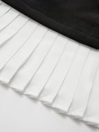 Asymmetric mini dress with white pleated hem, black waistband, and metallic accent detail.