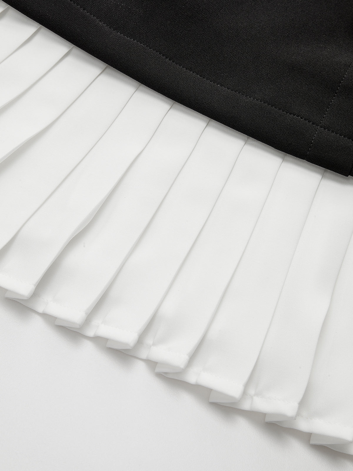 Asymmetric mini dress with white pleated hem, black waistband, and metallic accent detail.