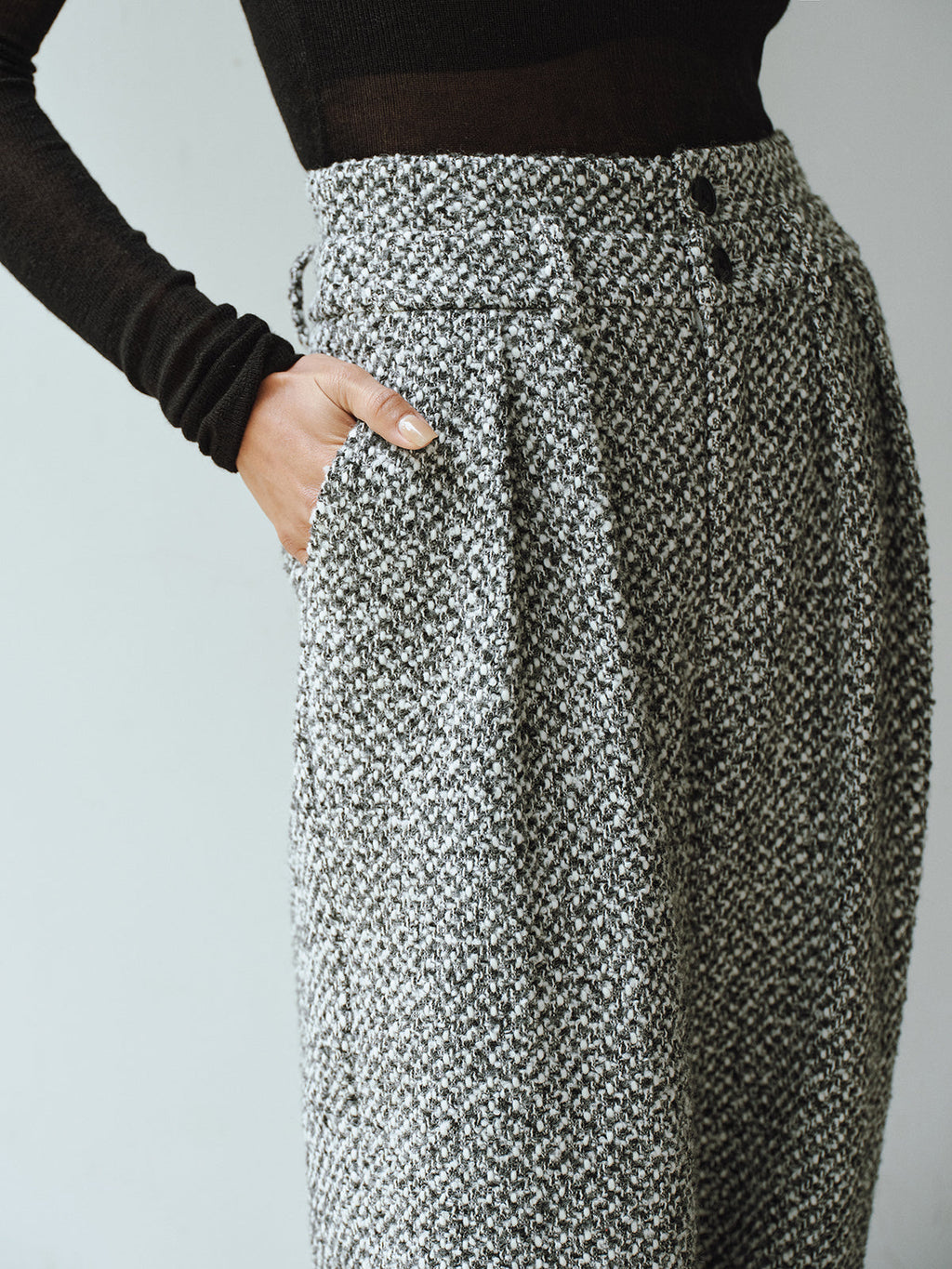 High-waisted, textured grey wool blend tweed trousers with black buttons and a black long-sleeve top.