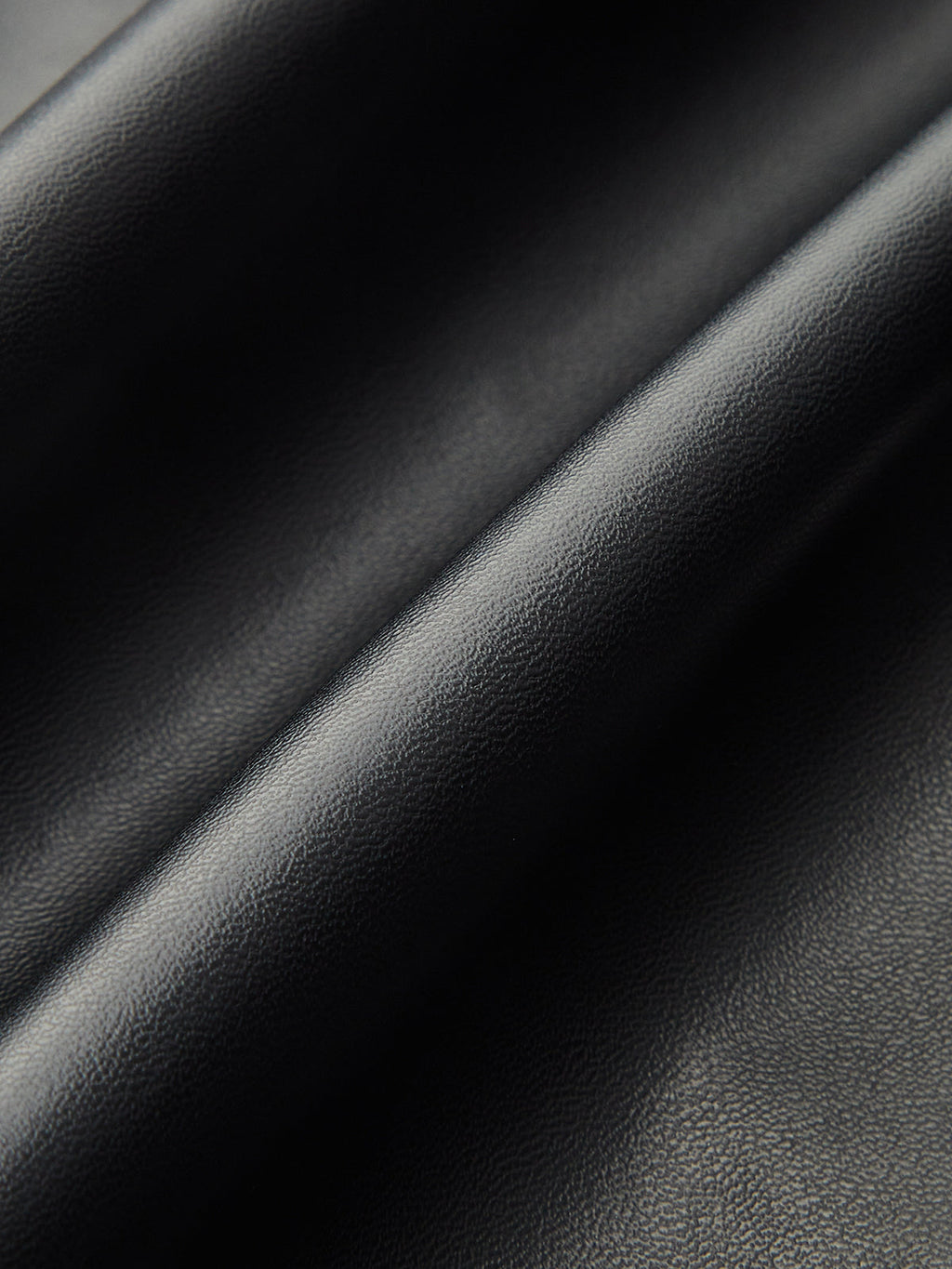 Close-up of black faux leather midi skirt, soft folds highlighting its glossy, textured finish.