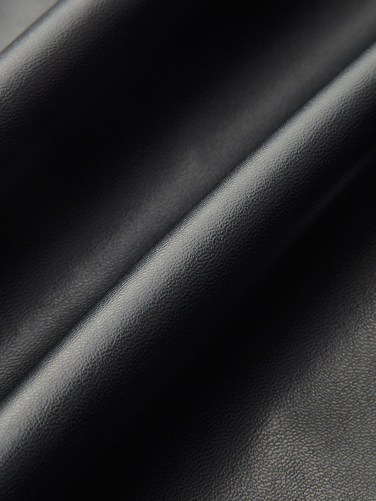 Close-up of black faux leather midi skirt, soft folds highlighting its glossy, textured finish.