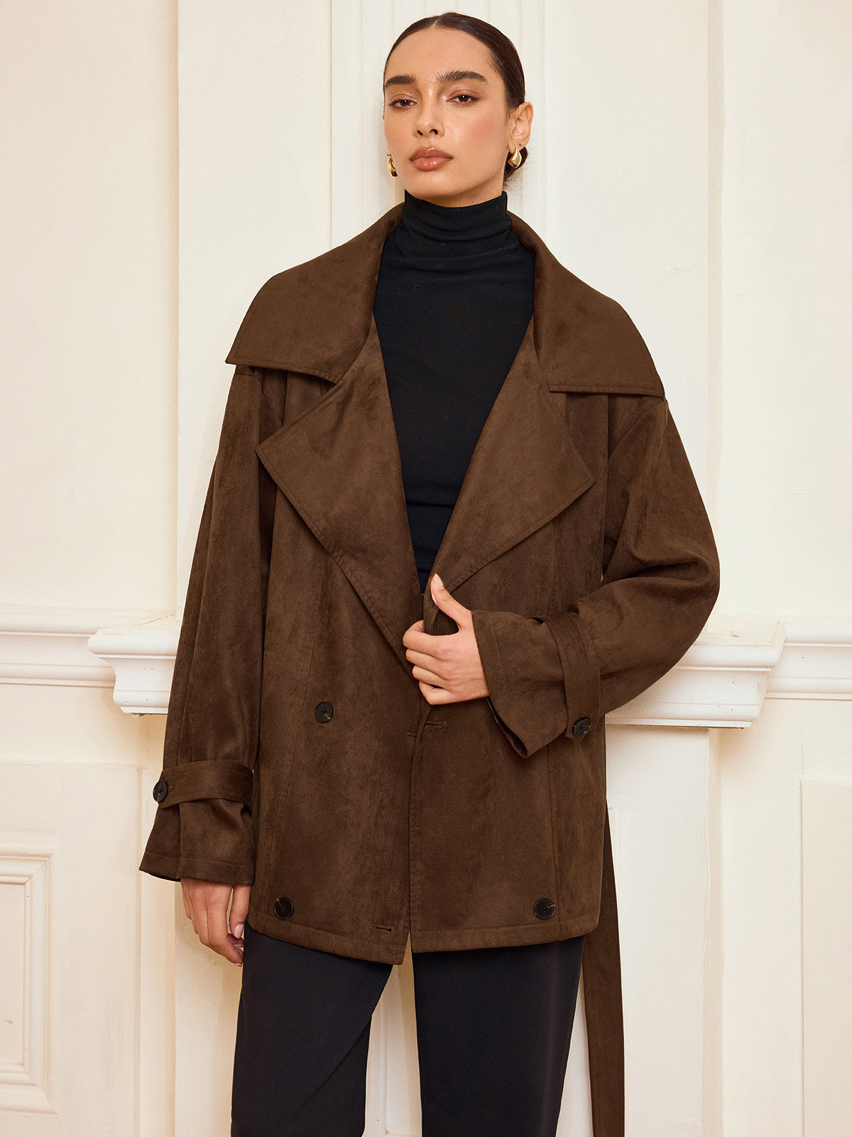 A suede-like trench coat with belt and lapel layered over a black turtleneck and pants.