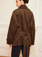 LA FINE FLEUR’s brown suede-like trench coat with belt and lapel, dark pants.
