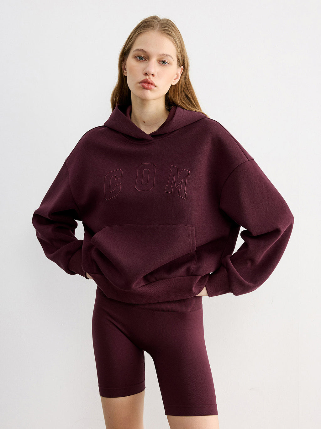 A casual hoodie with embroidered lettering, paired with matching maroon cycling shorts.