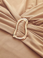 Beige deep V-neck bodysuit with long sleeves and a gold buckle gathering the center.