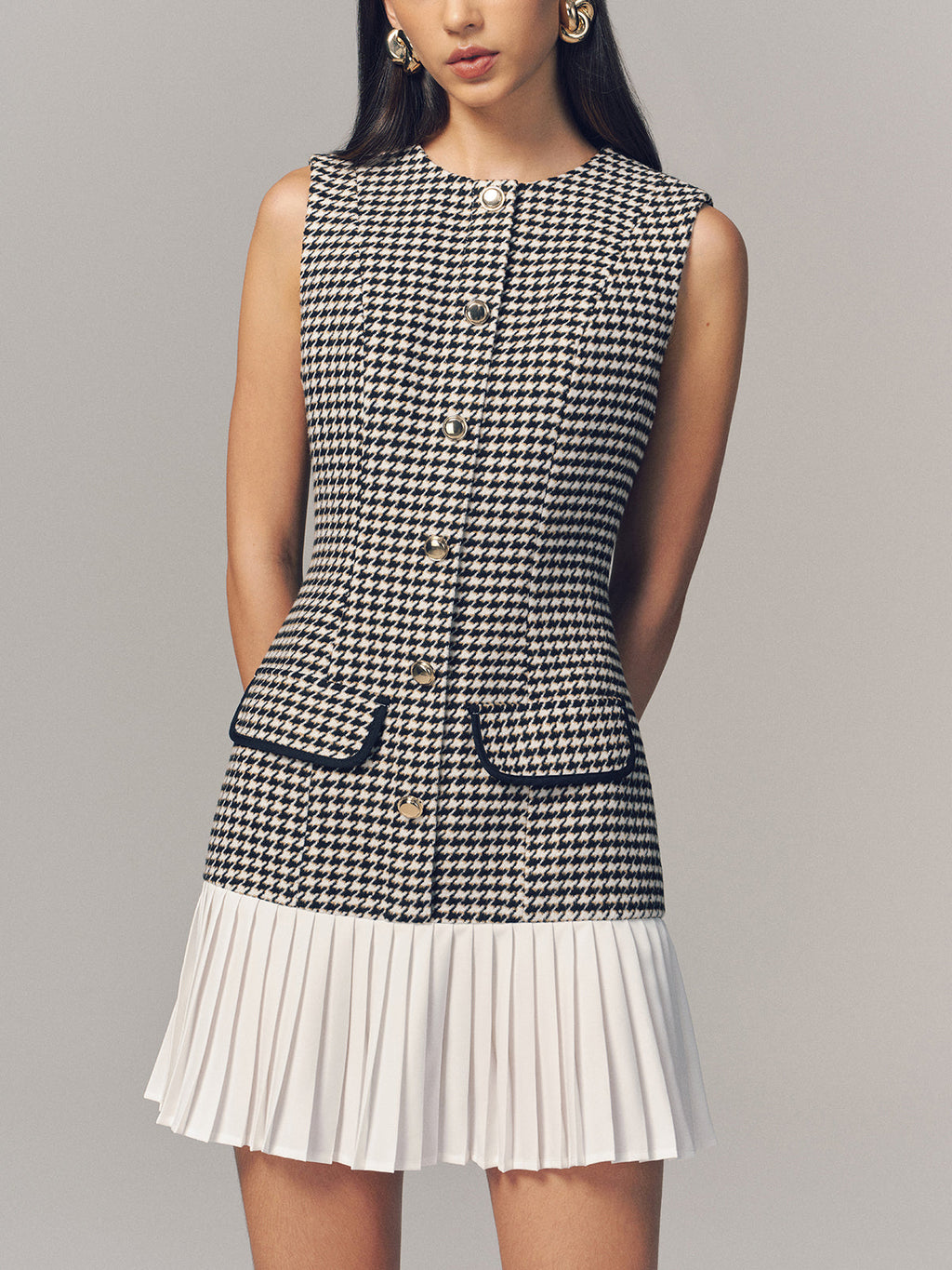 A houndstooth sleeveless mini dress with a pleated hem and gold button accents.