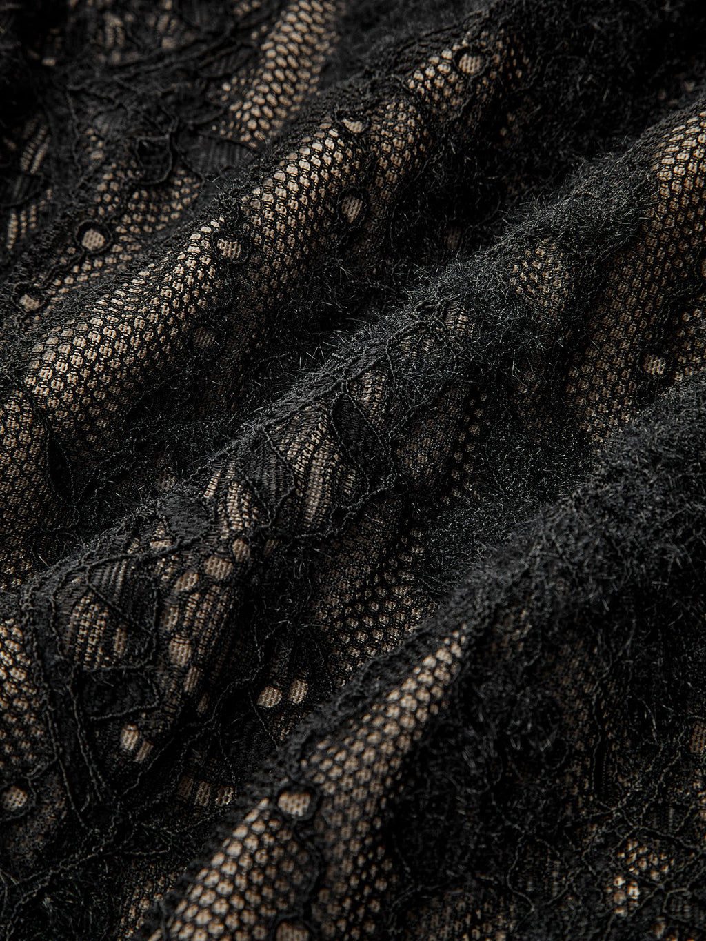 Black sheer lace bodysuit with floral and geometric patterns layered over beige fabric.