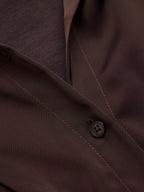 Brown suit jacket with black button, detailed stitching and textured weave, paired with satin bodysuit.