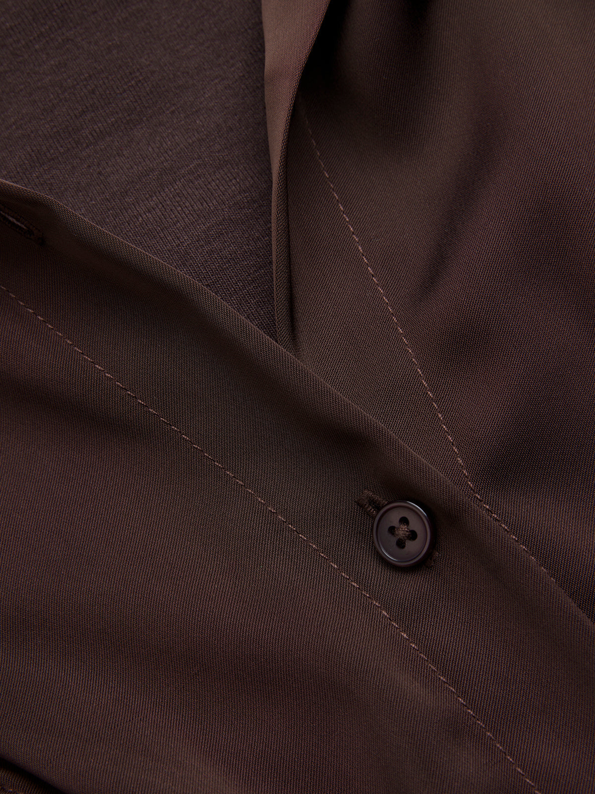 Brown suit jacket with black button, detailed stitching and textured weave, paired with satin bodysuit.