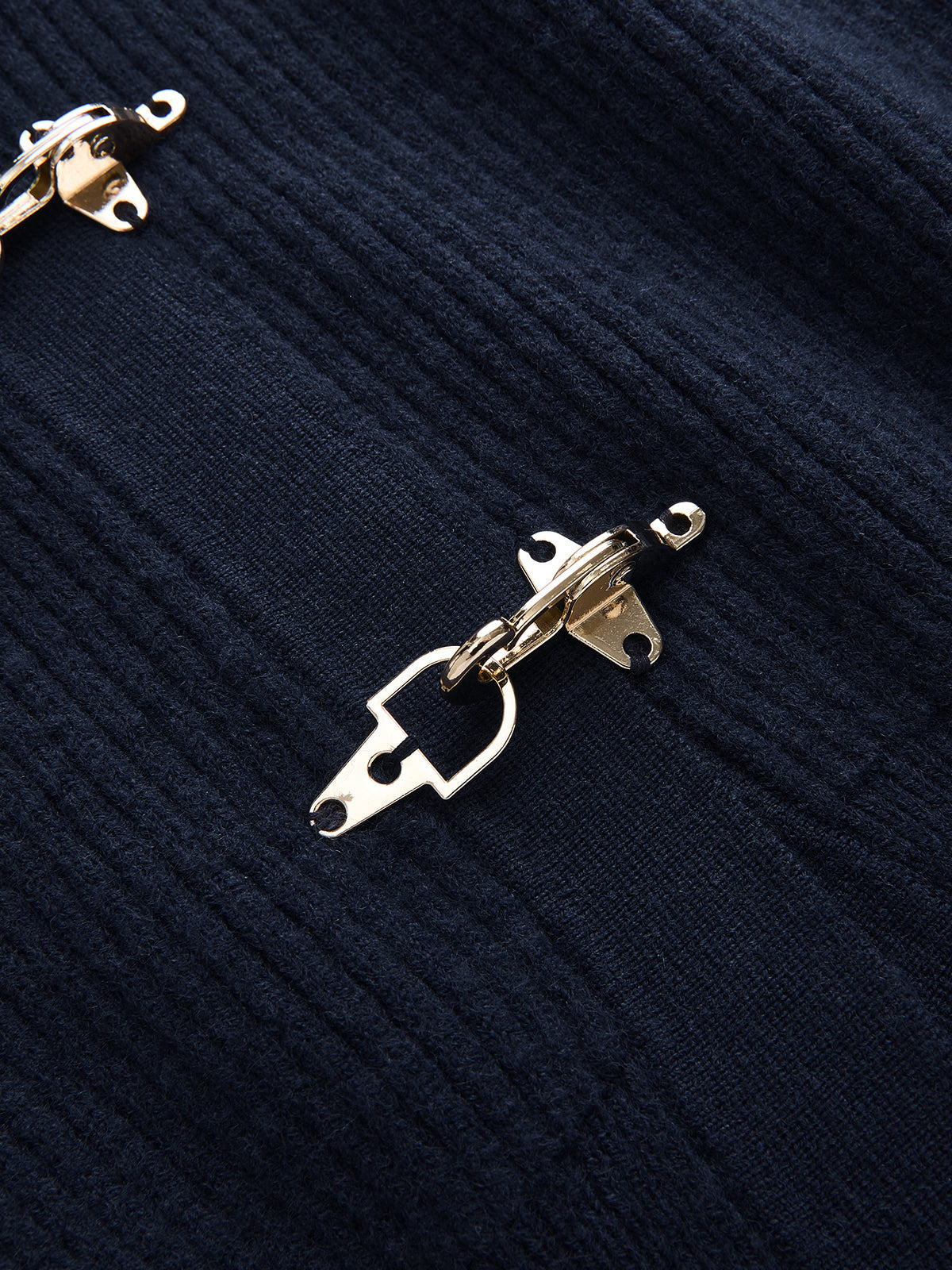 Gold metal clasp closure on dark navy knit vest with contrast trim and vertical ribbing.