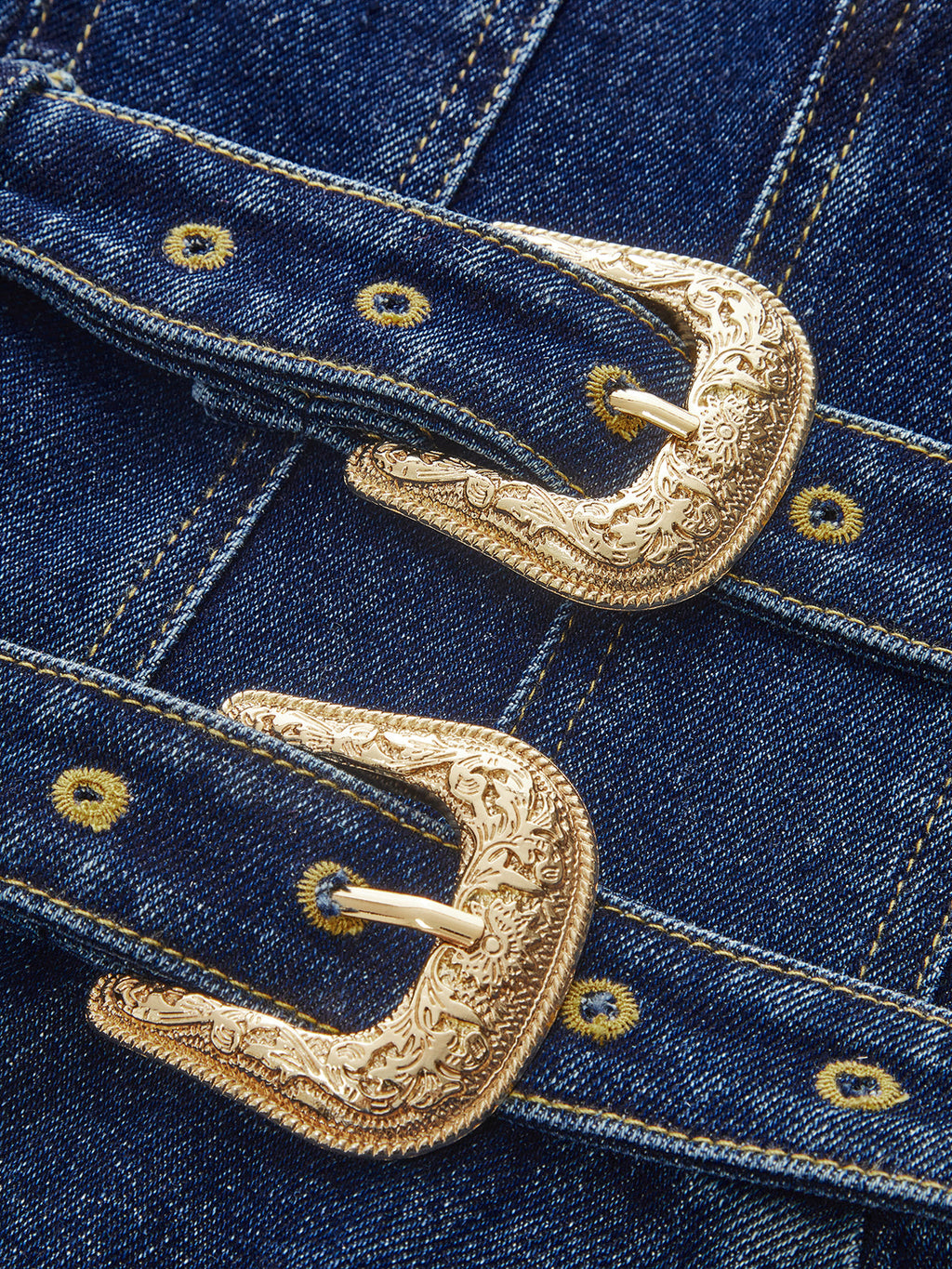 Denim mini dress with ornate gold dual buckles, yellow stitching, and metal rivet detailing.