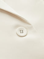 Cream blazer lapel with fabric-covered button and four silver eyelets, highlighting tailored texture.