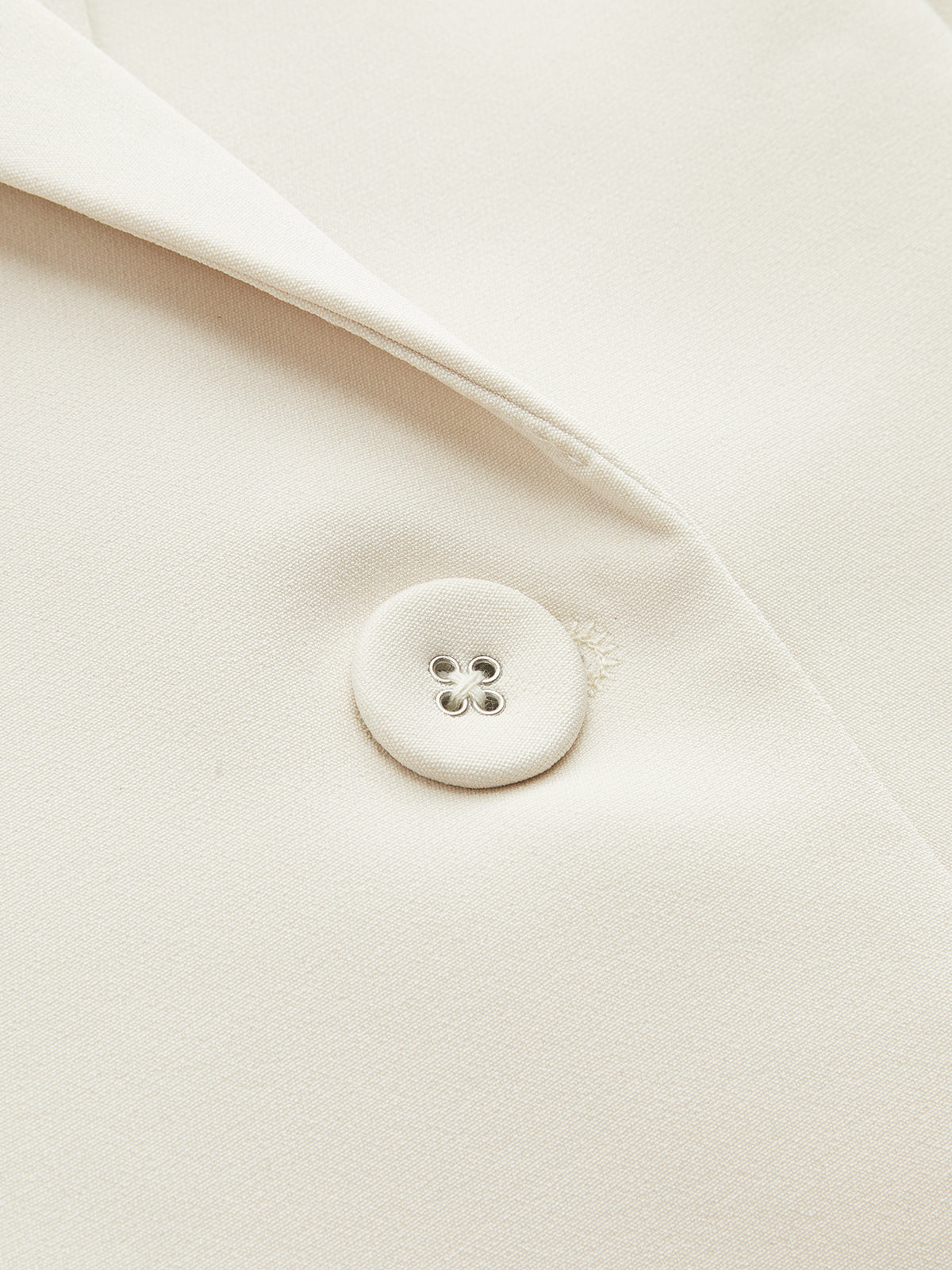 Cream blazer lapel with fabric-covered button and four silver eyelets, highlighting tailored texture.
