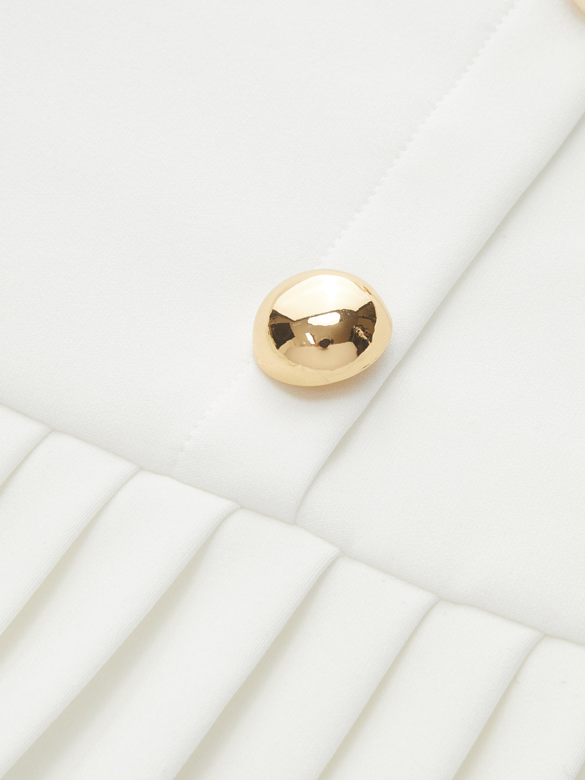 White pleated mini dress with a shiny gold metal accent at the neckline.