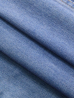 Close-up of blue denim shirt dress fabric, showing diagonal folds and visible stitching.