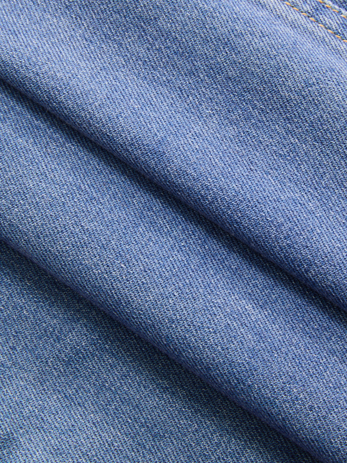 Close-up of blue denim shirt dress fabric, showing diagonal folds and visible stitching.