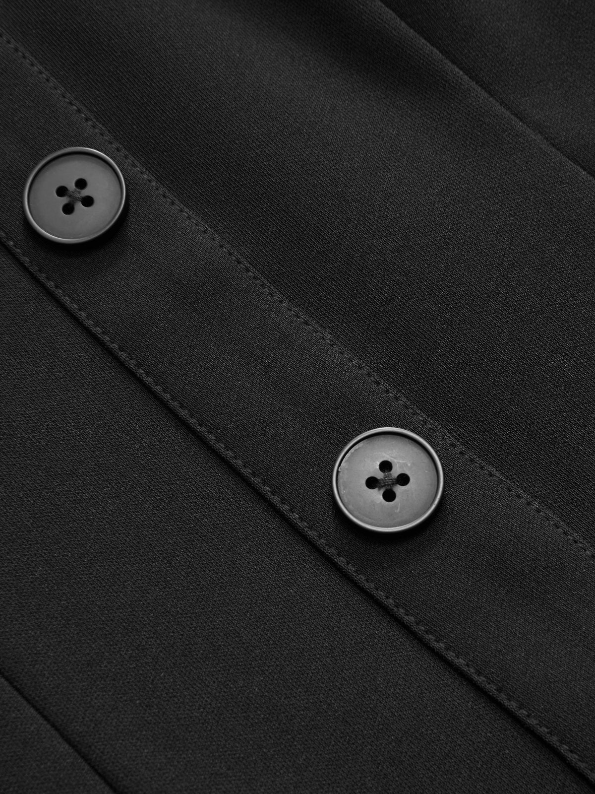 Close-up of black fabric dress with two black buttons, visible stitching, and party texture.