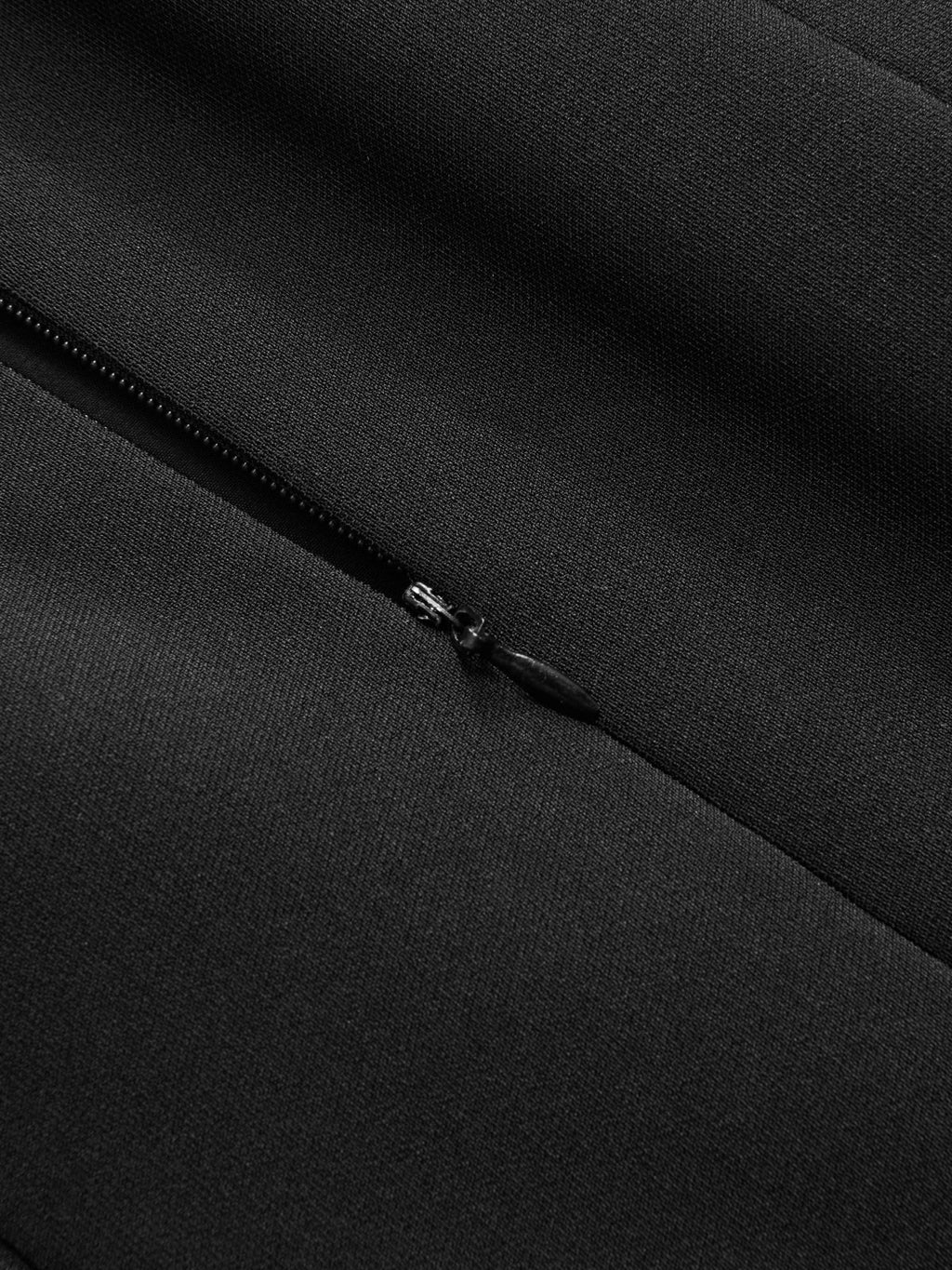Black zipper detail with metal pull on textured fabric, part of a flared hem dress.