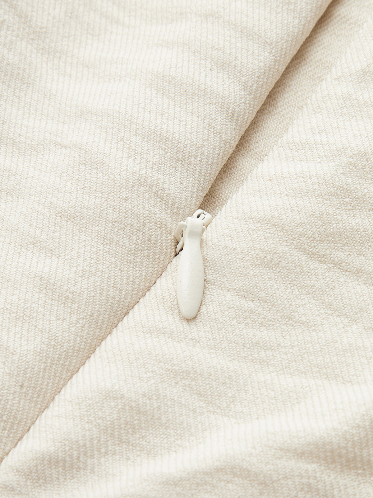 Close-up of white zipper on off-white one-shoulder jumpsuit with ruffle and contrast piping.