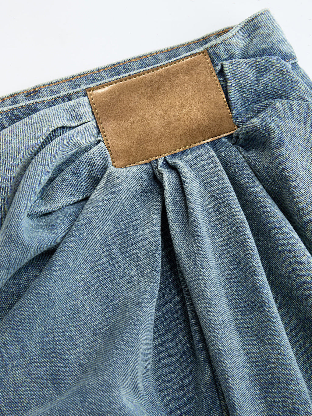 Ruched wide-leg jeans with an asymmetrical cut, gathered waistband, and brown leather back patch.