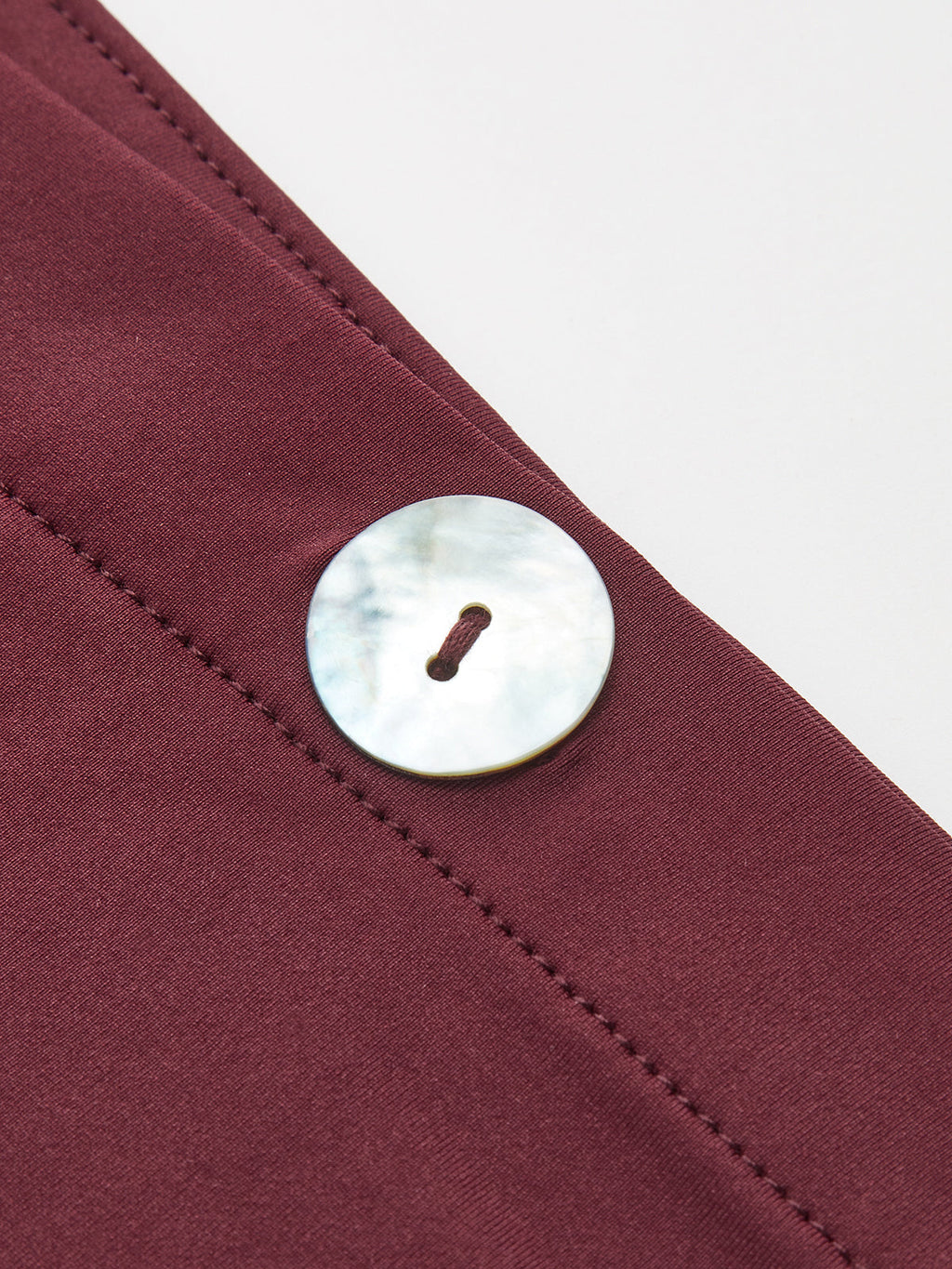 One-shoulder maroon top with visible stitching and a large, round mother-of-pearl button.