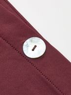 One-shoulder maroon top with visible stitching and a large, round mother-of-pearl button.