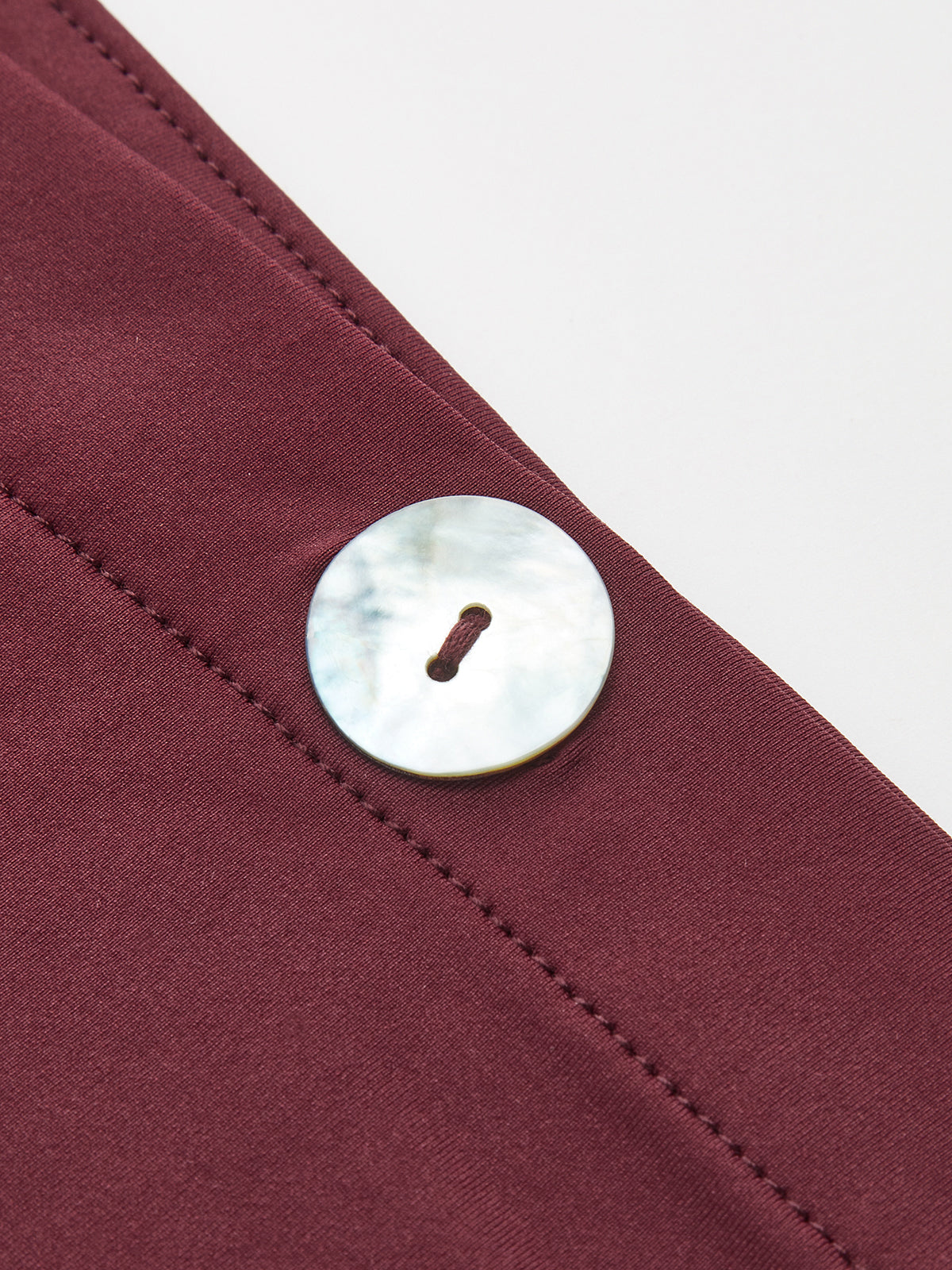 One-shoulder maroon top with visible stitching and a large, round mother-of-pearl button.