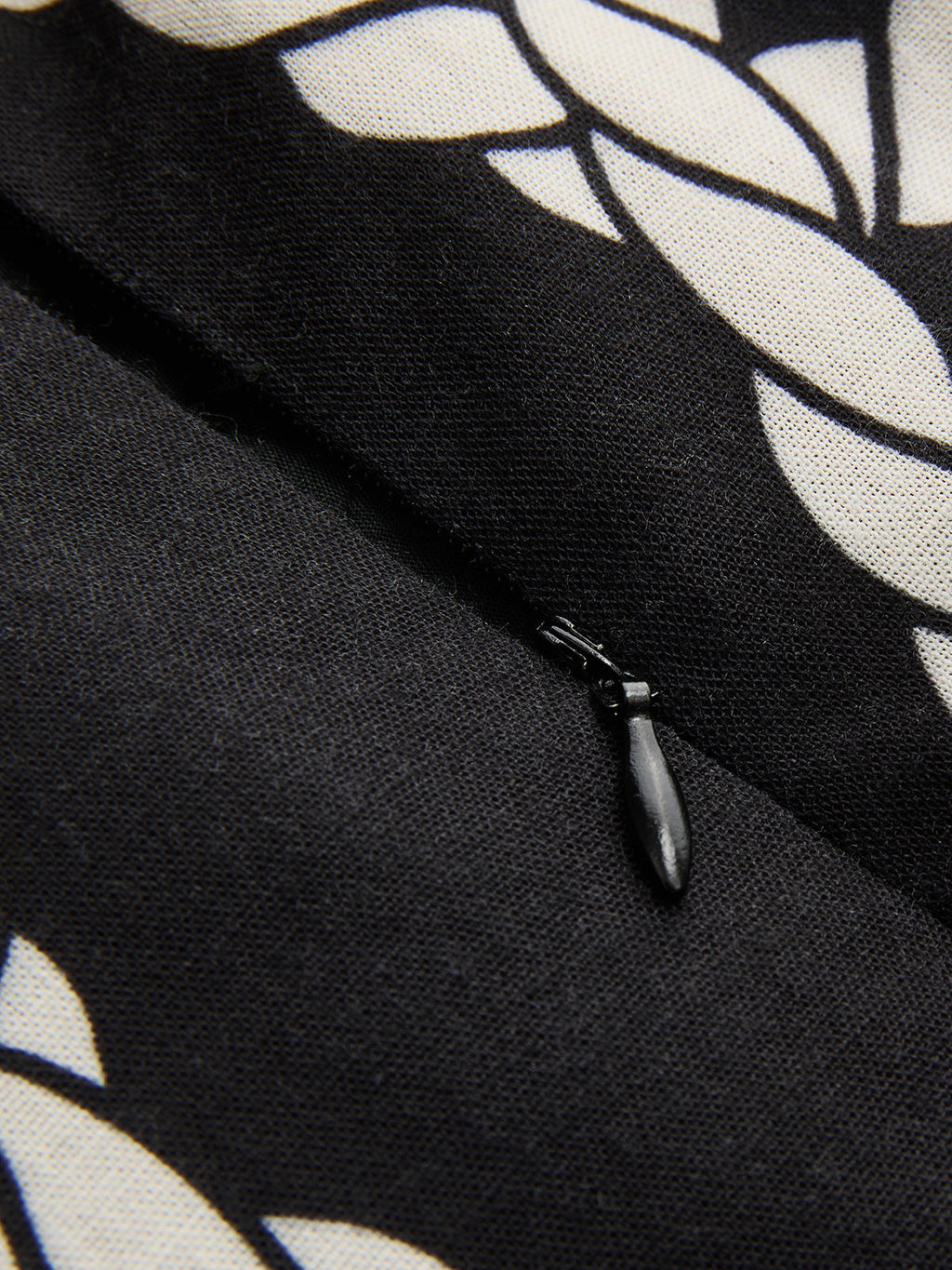 Black zipper and textured white leaf pattern on slim-fit camisole-style dress fabric.
