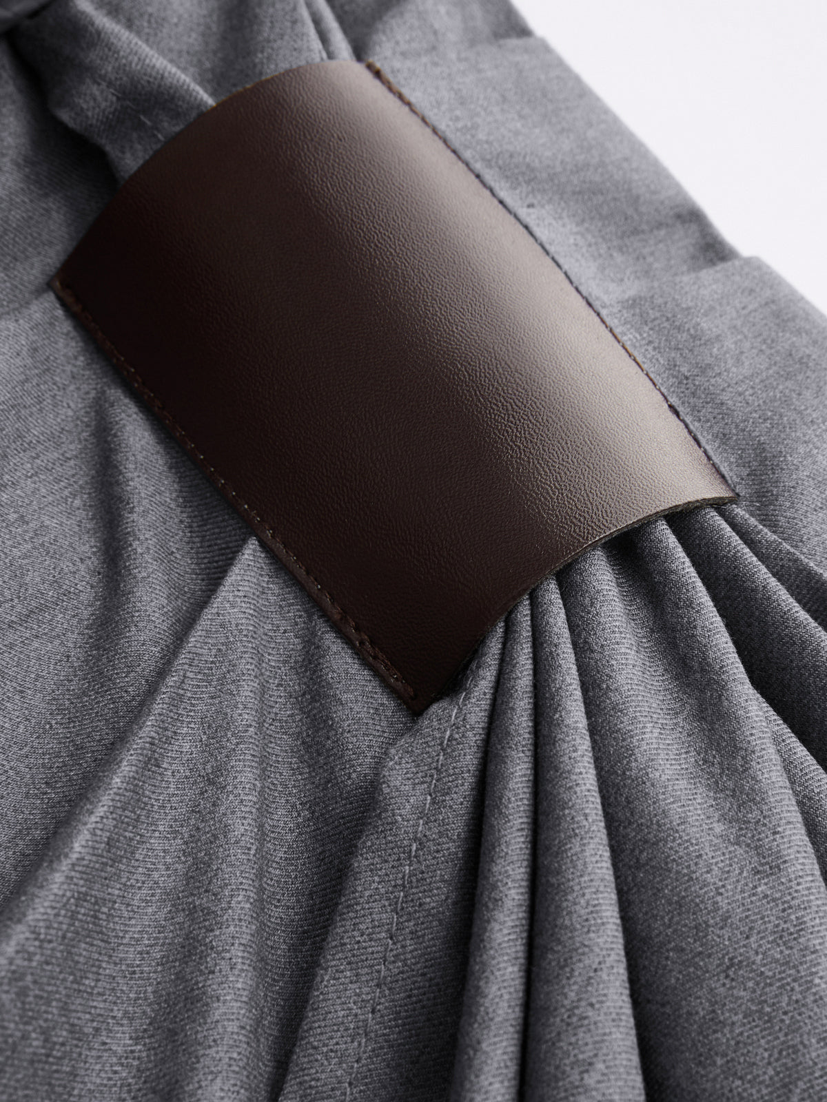Gray wrap-style wide-leg trousers featuring a dark brown leather strap with visible stitching.
