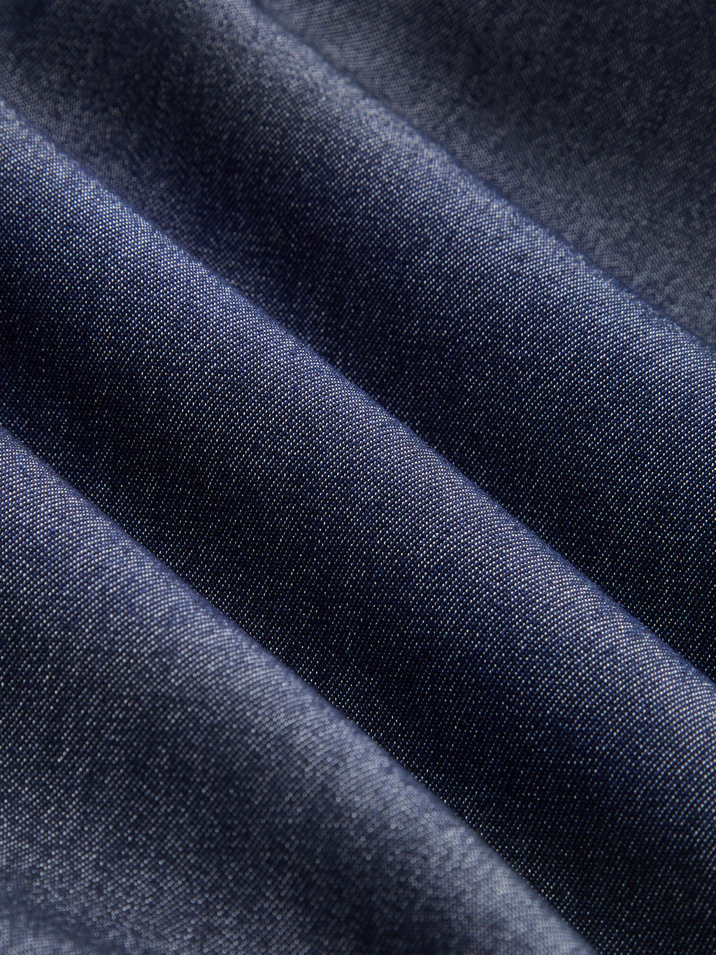 Dark blue sleeveless belted denim maxi dress with button details, diagonal folds, subtle sheen.
