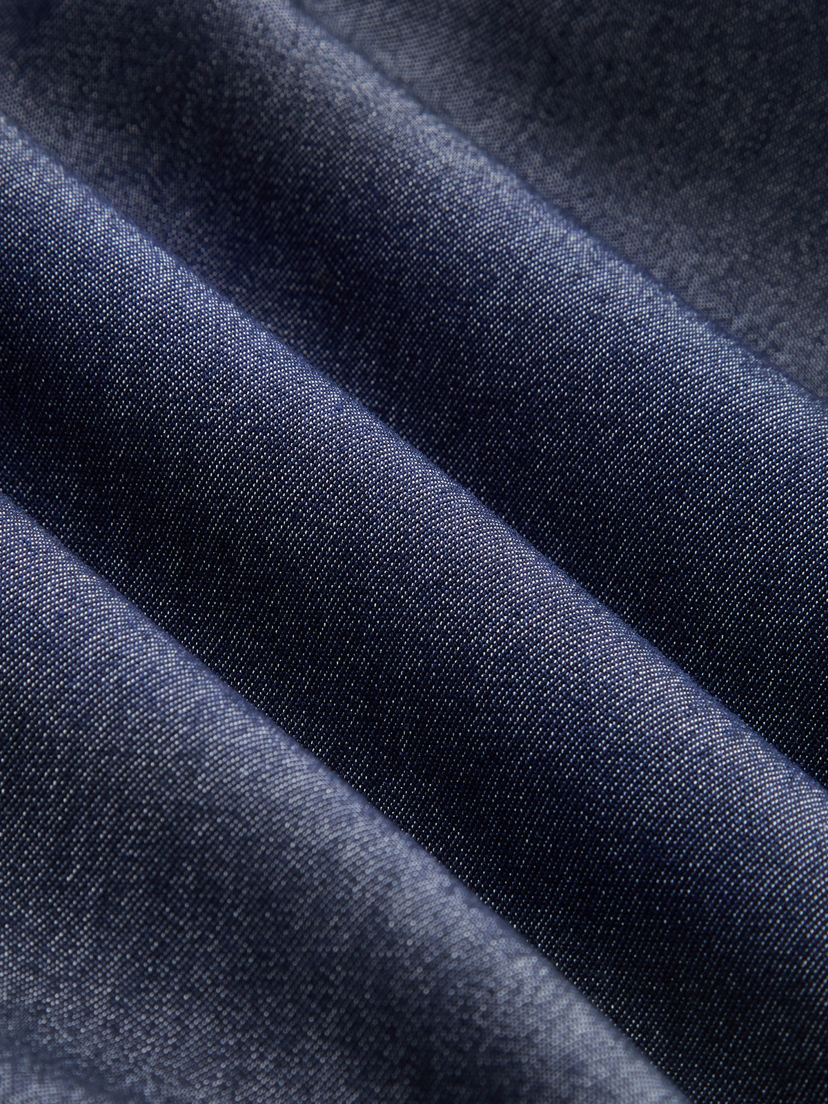 Dark blue sleeveless belted denim maxi dress with button details, diagonal folds, subtle sheen.