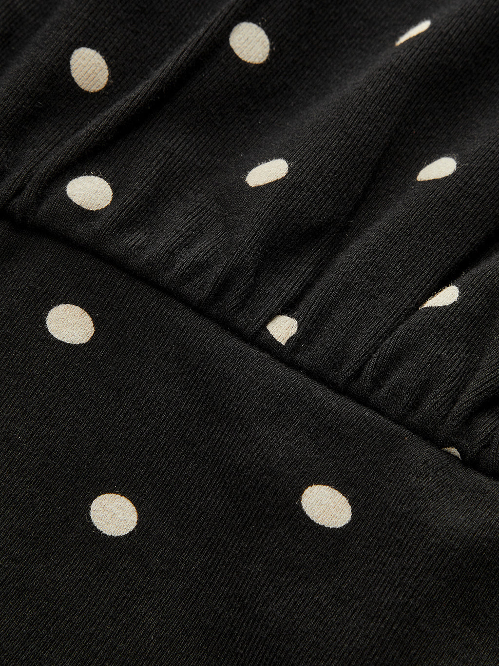 Black batwing top with off-white polka dots, diagonal ribbing, crew neck, cinched waist.